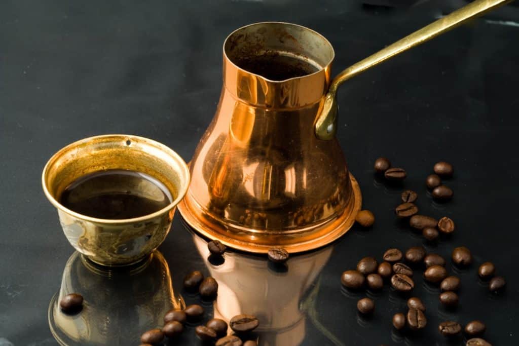 Copper cezve next to a small cup of Turkish coffee and coffee beans