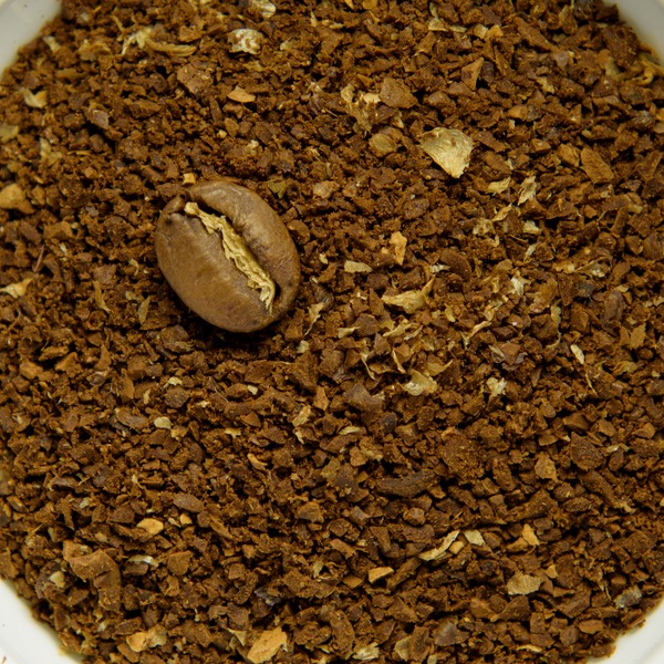 Coarse ground coffee in a white bowl, with a whole roasted bean for scale