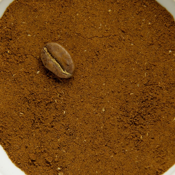 Fine ground coffee in a white bowl, with a whole roasted bean for scale