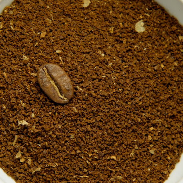 Medium-coarse ground coffee in a white bowl, with a whole roasted bean for scale