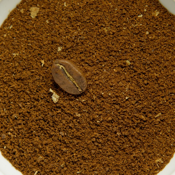 Medium ground coffee in a white bowl, with a whole roasted bean for scale