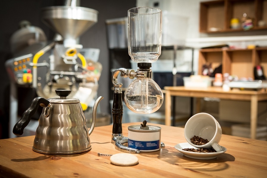 Hario siphon coffee maker with a gooseneck kettle, burner and coffee beans on a wooden counter
