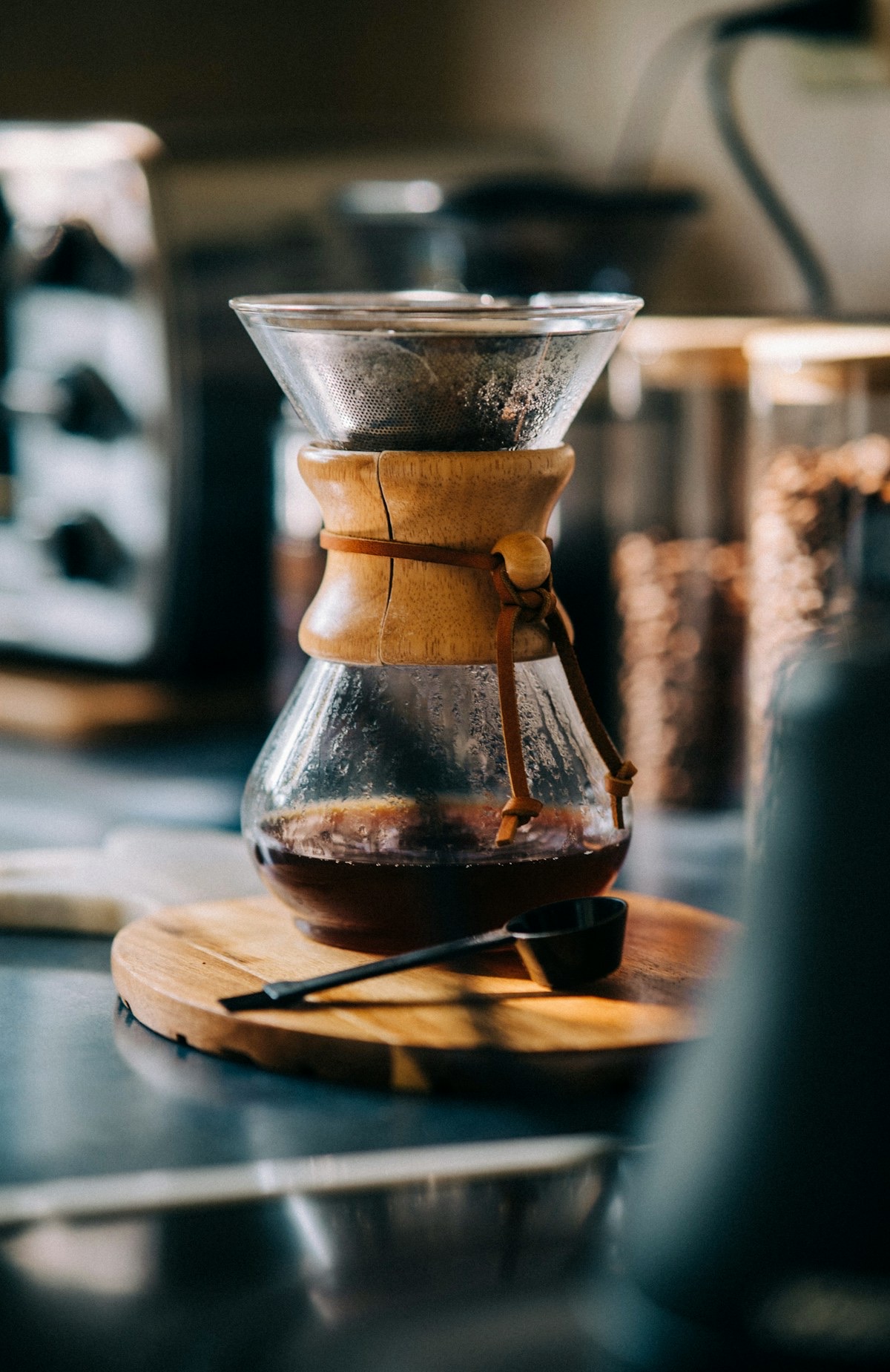 A Chemex of freshly brewed coffee on a wooden board with a coffee scoop