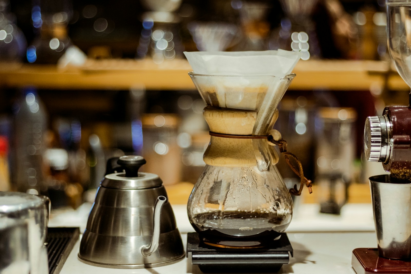 Chemex on a scale next to a gooseneck kettle and a coffee grinder