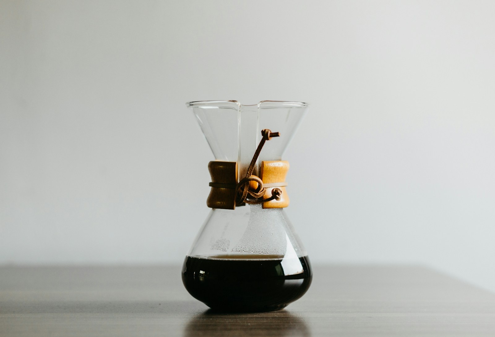 A Chemex coffeemaker with a wooden collar and leather tie, filled with brewed coffee