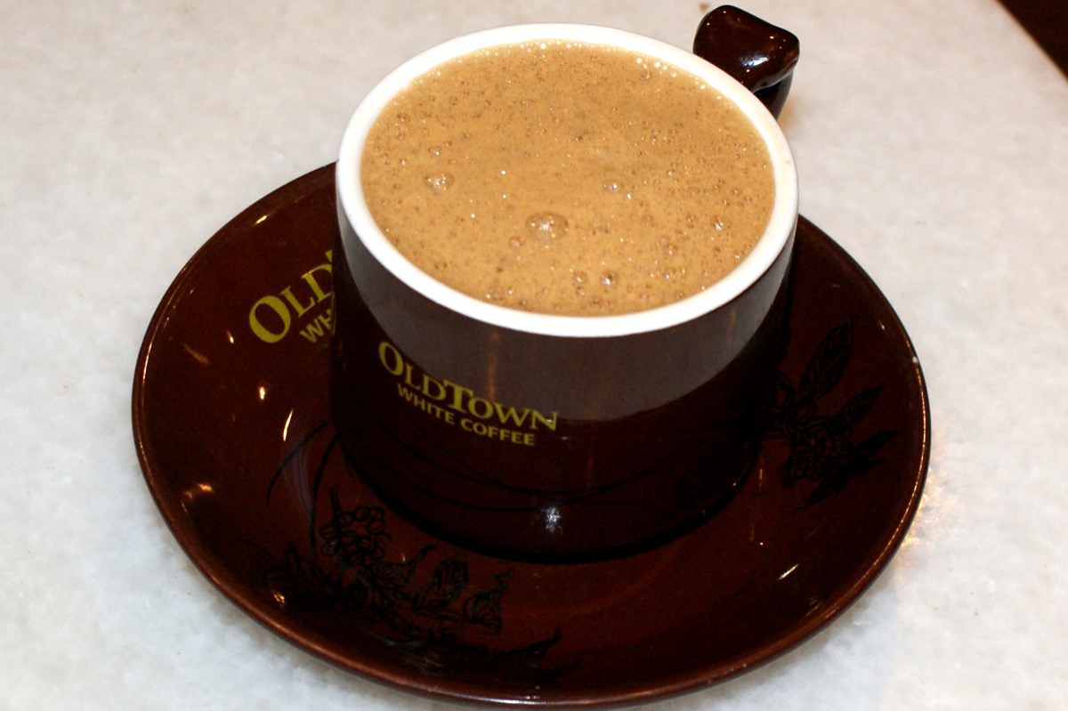 A cup of frothy, milky Ipoh white coffee in a brown OldTown White Coffee cup and saucer