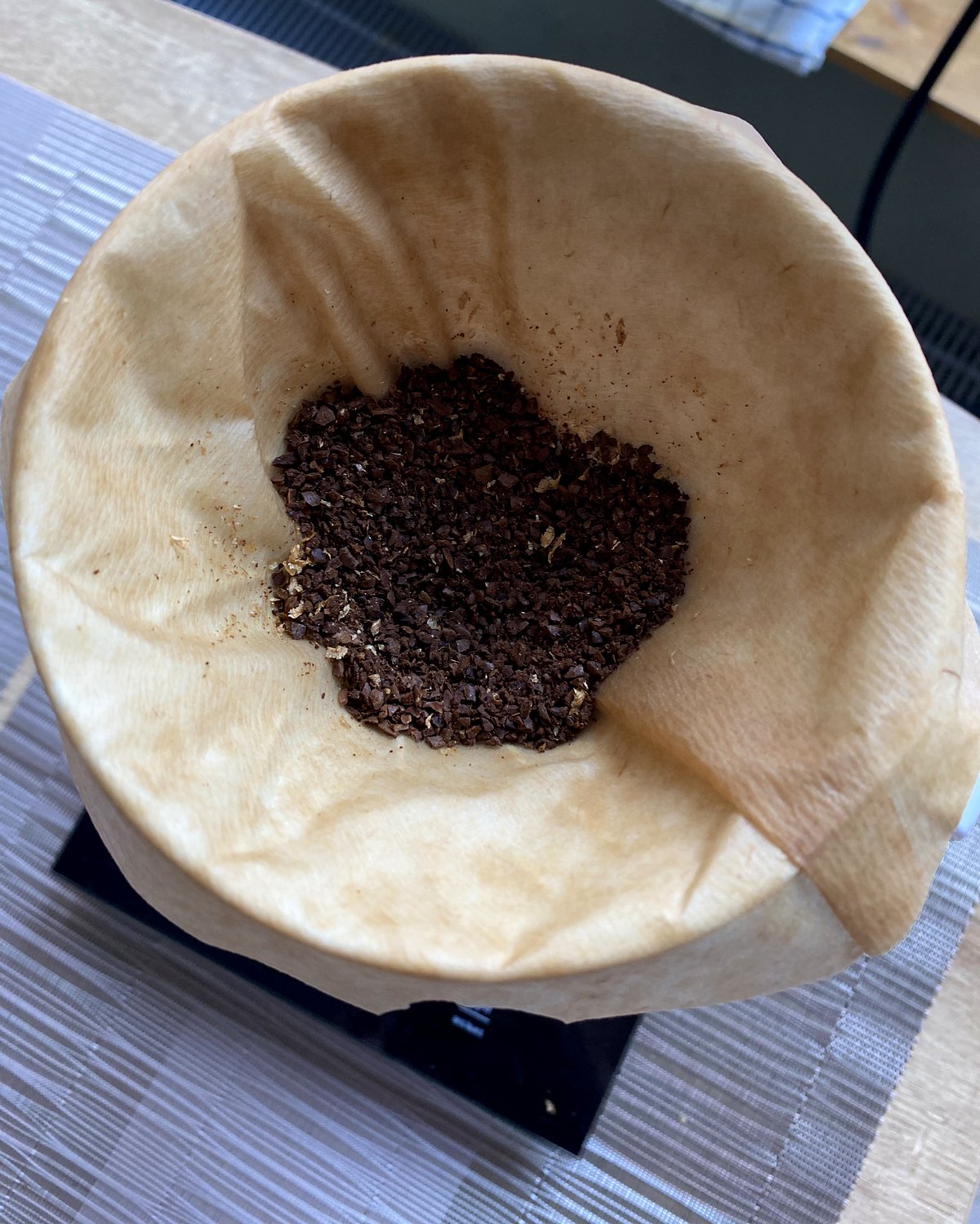 Natural brown Melitta paper filter in a V60 dripper on a scale, with ground coffee in the bottom