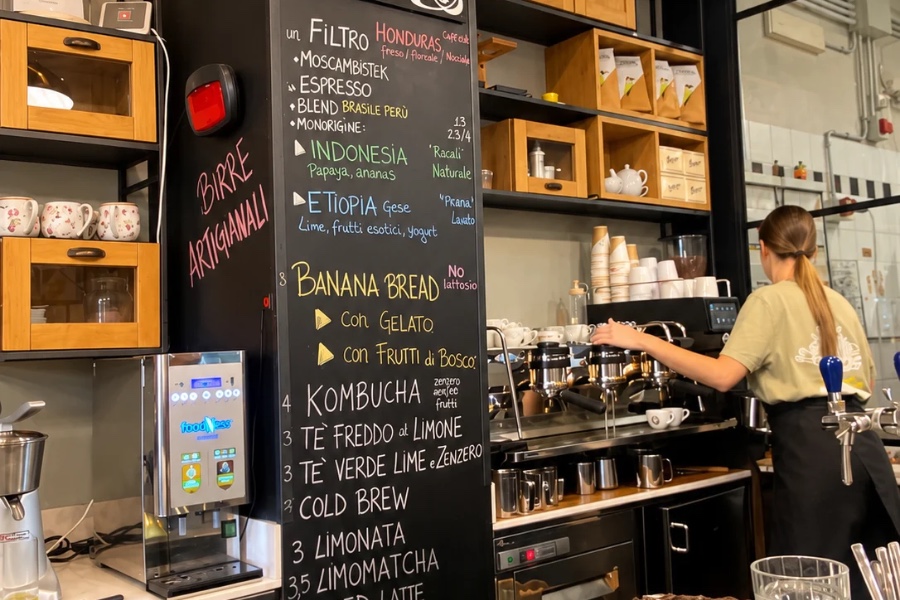Nero Vaniglia's chalkboard listing a Honduras on filter, a Brazil and Peru espresso blend and single origins from Indonesia and Ethiopia, with a barista at the espresso machine