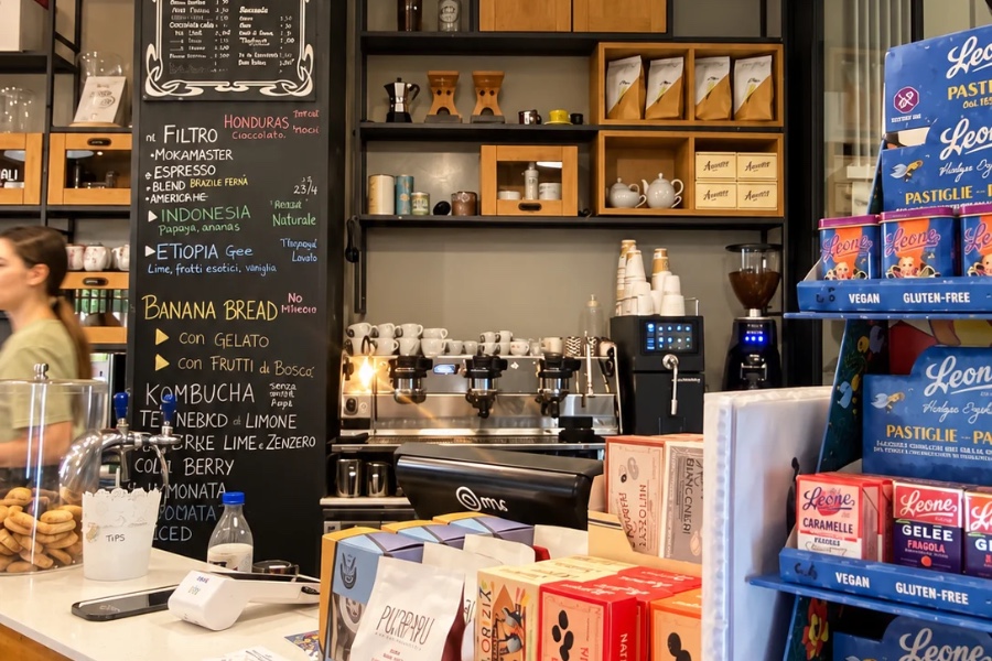 Nero Vaniglia's counter: chalkboard menu, shelves with V60 stands, a three-group espresso machine, a milk steaming unit and a grinder, with packaged sweets on the counter