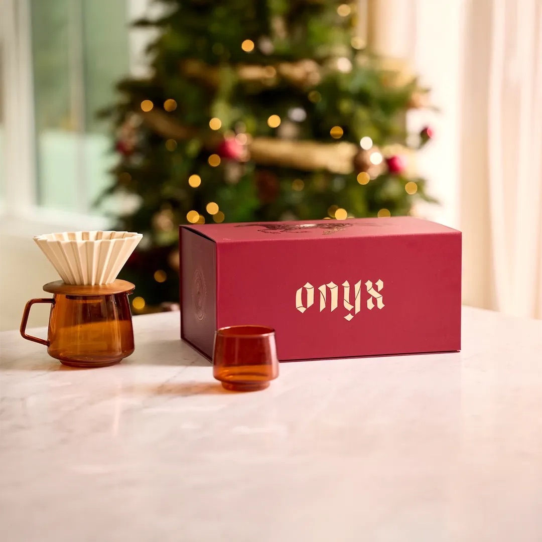 The red Onyx Coffee Lab advent calendar box on a marble table beside an amber glass dripper and cup, with a Christmas tree behind