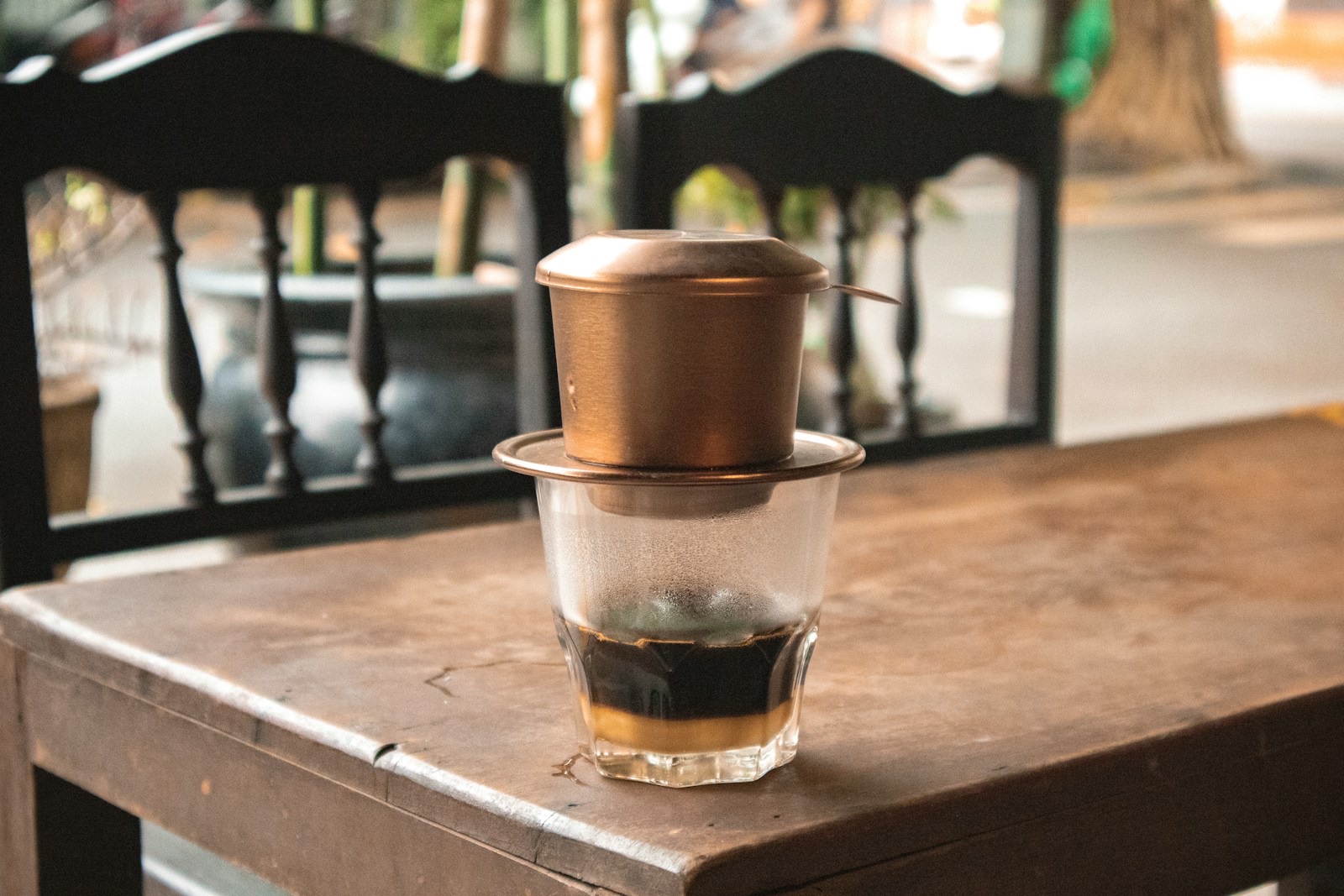 A phin filter dripping coffee into a glass with a layer of sweetened condensed milk