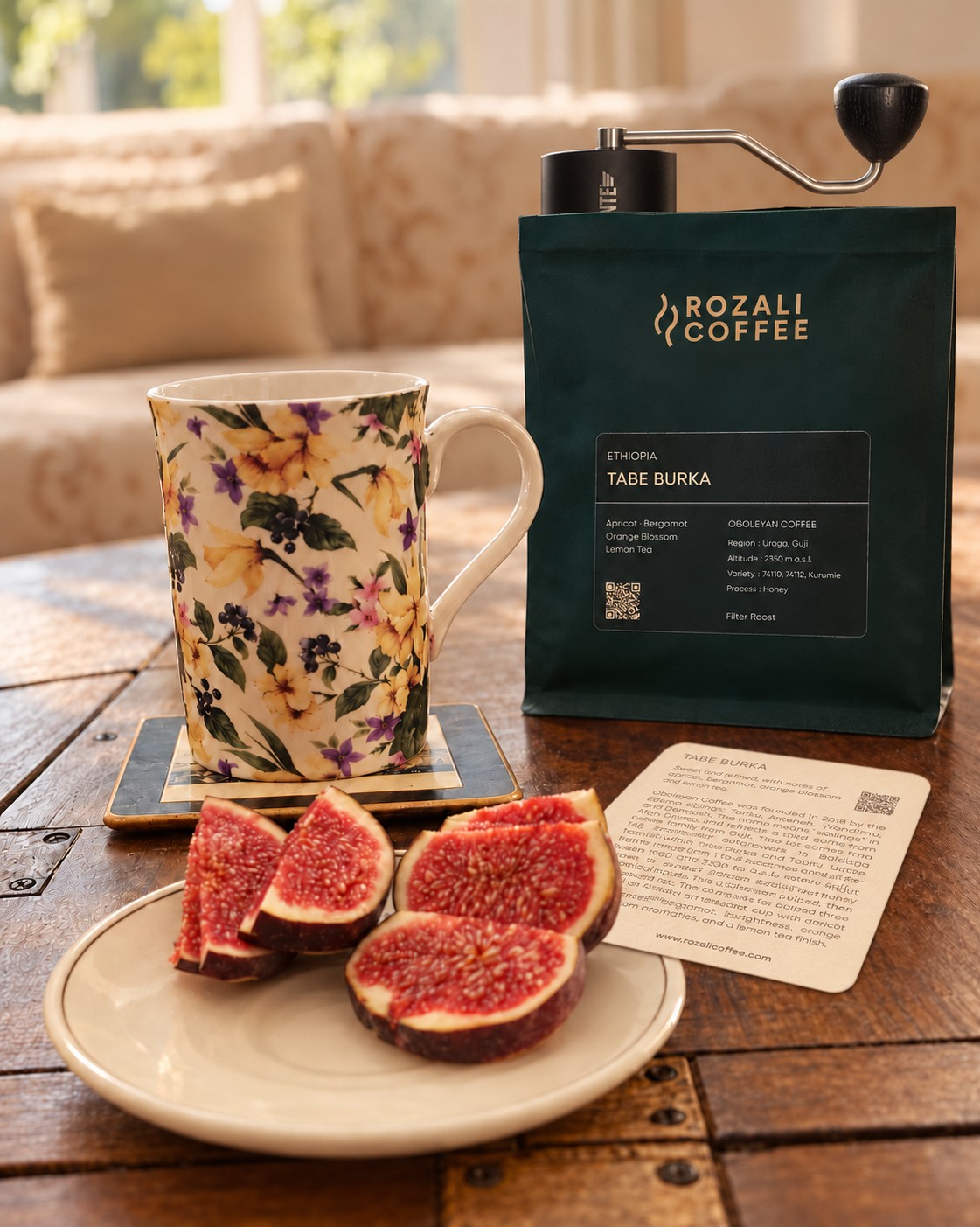 Rozali Coffee Tabe Burka bag with its lot card, a Comandante grinder, a floral mug and sliced figs on a wooden table