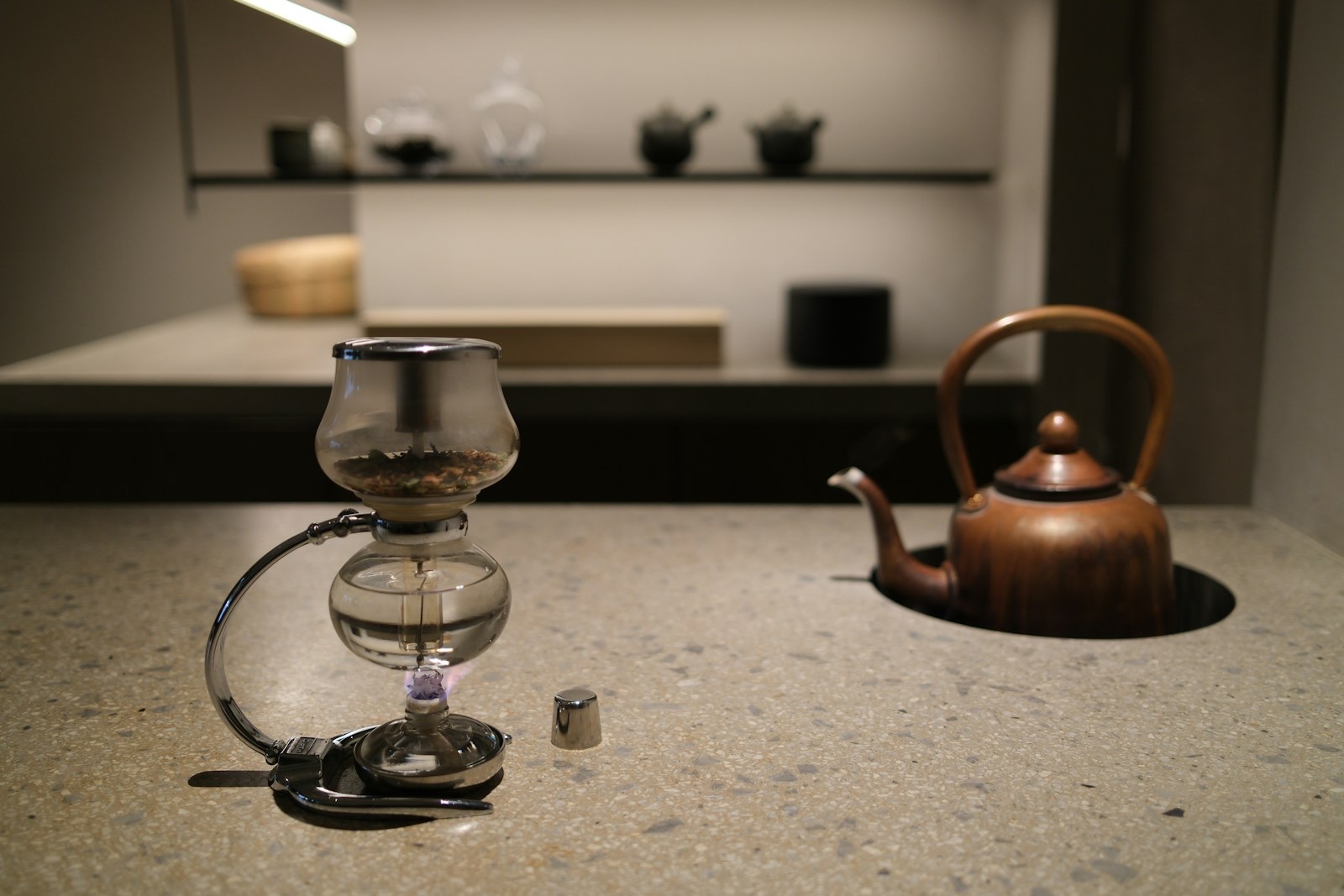 A siphon coffee maker brewing over a small burner next to a copper kettle