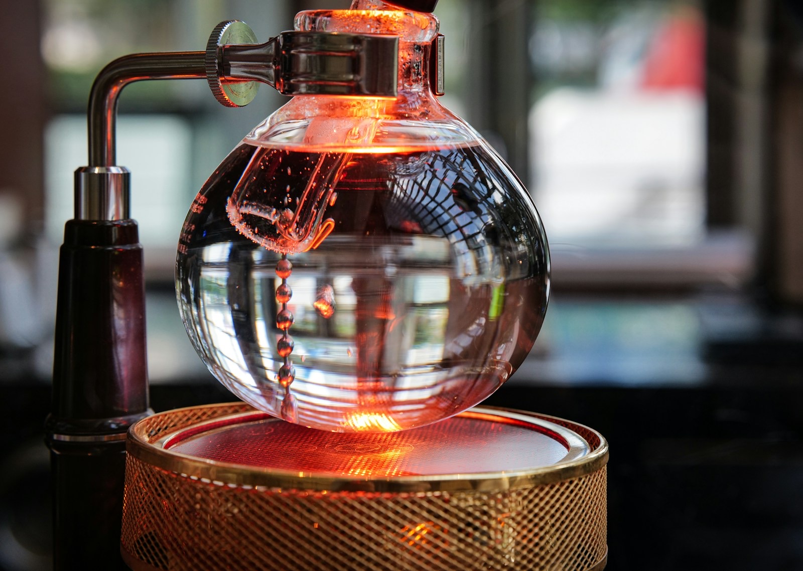 Siphon coffee maker lower bowl heating on a halogen beam heater, with the filter chain bubbling