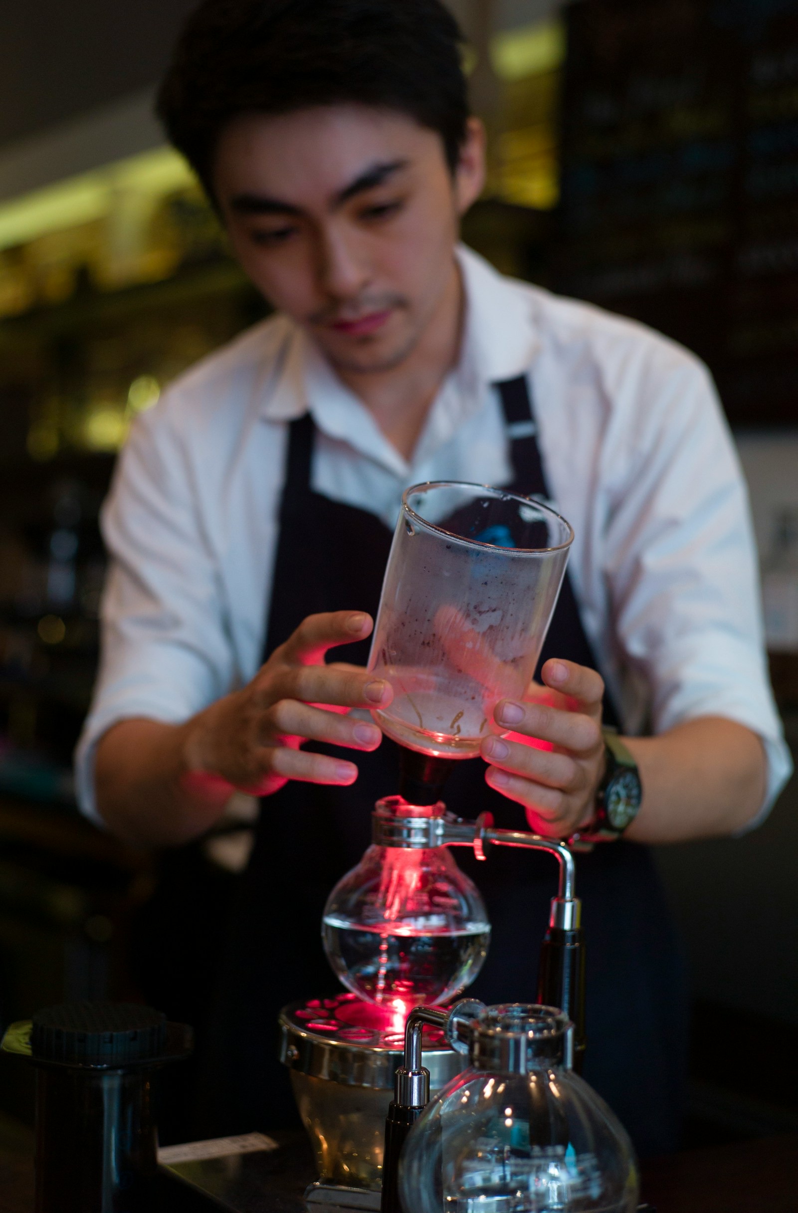 Barista fitting the upper chamber of a siphon coffee maker over a halogen heater