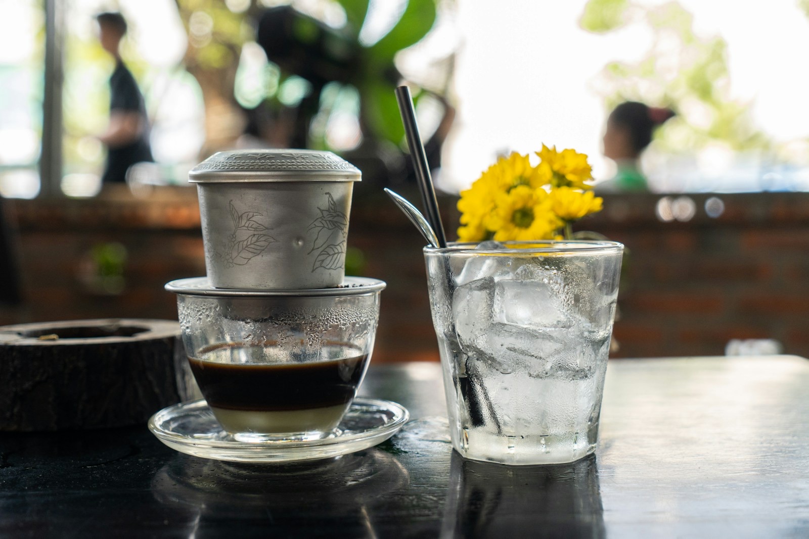 A phin filter dripping Vietnamese coffee into a glass, next to a glass of ice